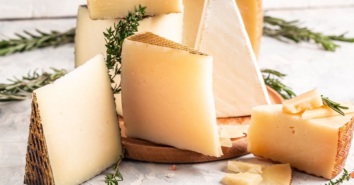 Spanish cheeses with dried herbs on wooden board on countertop.